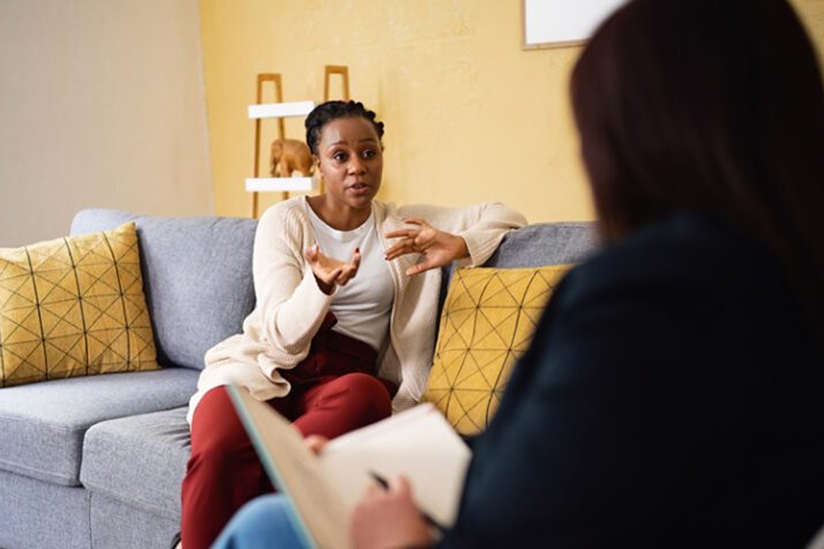 Person speaking with a therapist during a counseling session, expressing thoughts while the therapist listens and takes notes.